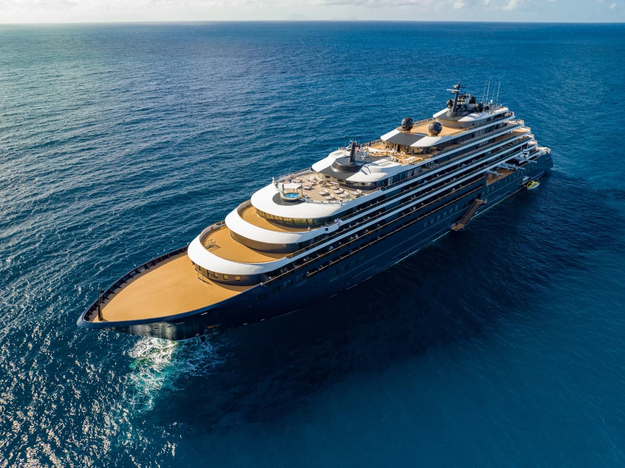 Aerial photograph of a Ritz-Carlton Yacht Collection superyacht sailing across deep blue water.